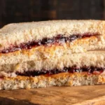 A perfectly toasted Peanut Butter and Jam Sandwich cut in half, showing layers of creamy peanut butter and fruity jam, served on a wooden board