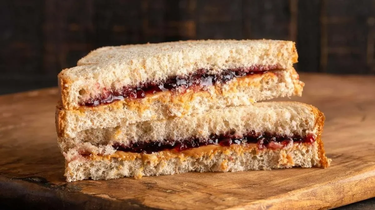 A classic peanut butter and jelly sandwich cut into halves, showing layers of creamy peanut butter and fruity jelly, served on a rustic wooden board